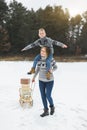 Young happy mother carrying her little son on shoulders, enjoying a sledge ride in a beautiful snowy winter park. Family Royalty Free Stock Photo