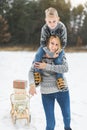 Young happy mother carrying her little son on shoulders, enjoying a sledge ride in a beautiful snowy winter park. Family Royalty Free Stock Photo