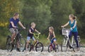 Young happy mother, father and two cute blond children, boy and girl riding bicycles on pebbled river bank on blurred bright summe Royalty Free Stock Photo