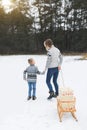 Young happy mother and her son enjoying a sledge ride in a beautiful snowy winter forest. Wooden sledge with present Royalty Free Stock Photo