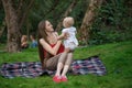 Young happy mother holding cute baby on nature background. Family picnic