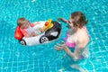 Young happy mother in a pink bikini having fun and catch baby in the pool. A joyful little child sits in an inflatable boat in the Royalty Free Stock Photo