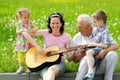 Young happy mother playing guitar for her young children and grandfather