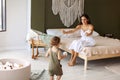 Young happy mother sitting on bed while her cute little boy son makig fisrt steps and learning to walk Royalty Free Stock Photo