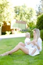 Young happy mother sitting with little baby on grass in yard. Royalty Free Stock Photo