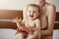 Young happy mother in sleepwear and her newborn baby sitting on bed in morning smiling playing together. Royalty Free Stock Photo