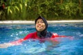 Young happy muslim woman playing with water excited in resort swimming pool splashing and having fun wearing traditional islam Royalty Free Stock Photo