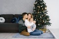 Young happy parents with a young son in his arms sitting at the Christmas tree. Husband kisses his wife