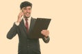 Young happy Persian businessman smiling and reading on clipboard while talking on mobile phone Royalty Free Stock Photo