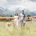 Young happy pregnant couple holding hands walking it`s Golden retriever dog outdoors in meadow. Royalty Free Stock Photo