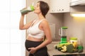 Happy pregnant woman drinking green protein cocktail