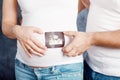 Young happy pregnant woman and her husband holding an ultrasonography photo. Close up on pregnant belly. Woman expecting a baby