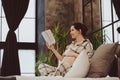 Young happy pregnant woman in pajama reading book and touching belly gently while relaxing at home Royalty Free Stock Photo