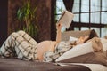 Young happy pregnant woman in pajama reading book and touching belly gently while relaxing at home Royalty Free Stock Photo