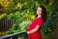 A young happy pregnant woman in a red dress with flowers in her hands is resting and enjoying life in nature Royalty Free Stock Photo