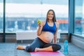 Happy pregnant woman sitting on yoga mat with apple while exercising at gym Royalty Free Stock Photo