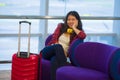 Young happy and pretty Asian Chinese tourist woman sitting at airport departure boarding gate waiting for flight using internet on Royalty Free Stock Photo