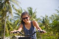 Young happy and pretty Asian Chinese woman riding bike in Vietnam or Thailand tropical jungle forest with palm trees smiling relax Royalty Free Stock Photo