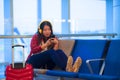 Young happy and pretty Asian Korean tourist woman sitting at airport departure boarding gate waiting for flight using internet on Royalty Free Stock Photo