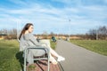 Young, happy redhead girl in the spring in the park near the river listens to music through wireless bluetooth headphones