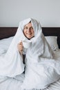 Young happy redhead woman with cup of coffee sitting in bed under blanket at home bedroom. comfort or home weeekend Royalty Free Stock Photo