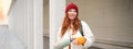 Young happy redhead woman in red hat, drinking from thermos, warming up with hot drink in her flask while walking around Royalty Free Stock Photo