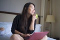 Young happy and relaxed Asian Korean woman at hotel room bed working with laptop computer eating apple cheerful in business travel Royalty Free Stock Photo