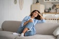 Young happy relaxed woman sitting on sofa enjoying quiet moments at home with cup of tea or coffee Royalty Free Stock Photo