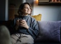 Young happy  relaxed woman in warm sweater holding mug of coffee while sitting on sofa at home Royalty Free Stock Photo