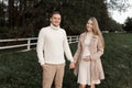 Young happy romantic pregnant couple is walking holding hands outdoors at autumn warm day. Pregnant woman in knit dress Royalty Free Stock Photo