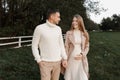 Young happy romantic pregnant couple is walking holding hands outdoors at autumn warm day. Pregnant woman in knit dress Royalty Free Stock Photo