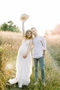 Young happy romantic pregnant couple walking in wild field in summer day. Pregnant woman in white dress and her handsome Royalty Free Stock Photo