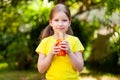 Young happy school age child, little girl holding an opened glass bottle full of nutritious orange colored vegetable juice Royalty Free Stock Photo