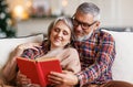 Young happy senior family couple in love enjoying Christmas holidays together at home, reading book Royalty Free Stock Photo