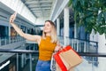 Young happy after shopping woman talking on cell in mall. Satisfied joyful female shopaholic with gift colored paper bags in hands Royalty Free Stock Photo