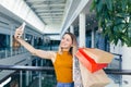 Young happy after shopping woman talking on cell in mall. Satisfied joyful female shopaholic with gift colored paper bags in hands Royalty Free Stock Photo