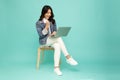 Young happy smiling Asian woman holding laptop computer and sitting on chair on green background.