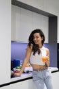 Young happy smiling attractive woman with dark hair standing in kitchen with glass of orange juice in the morning Royalty Free Stock Photo