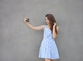 Young happy smiling beautiful woman in light dress with long brunette curly hair posing against wall on a warm Royalty Free Stock Photo