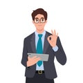 Young happy smiling businessman clerk manager character standing with tablet and showing ok sign