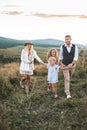 Young happy smiling family with two daughters having fun at countryside, walking in the field, holding hands and talking Royalty Free Stock Photo