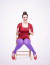 Young happy smiling girl in a red mini dress sits on a chair and shows size with hands, front view. Royalty Free Stock Photo