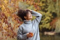 Young happy smiling mixed-race woman with coffee cup in autumn nature, pleased african american female with curly hair in knitted Royalty Free Stock Photo