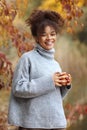 Young happy smiling mixed-race woman with coffee cup in autumn nature, pleased african american female with curly hair in knitted Royalty Free Stock Photo