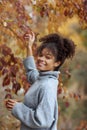 Young happy smiling mixed-race woman with coffee cup in autumn nature, pleased african american female with curly hair in knitted Royalty Free Stock Photo