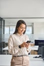 Happy professional Asian business woman using mobile phone in office, vertical. Royalty Free Stock Photo