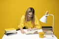 Young happy smiling student woman in yellow casual clothes reading the book at the table in library of university or Royalty Free Stock Photo