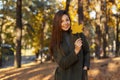Young happy smiling stylish girl in a fashionable green coat holding a golden autumn leaf walks in the park on a sunny day. Royalty Free Stock Photo