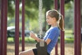 Young happy smiling teenager girl reading study homework on digital tablet during summer vacations sitting on swing in Royalty Free Stock Photo