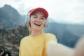 Young happy smiling woman backpacker with short brunette hair and yellow beanie, taking selfie with smartphone doing Royalty Free Stock Photo